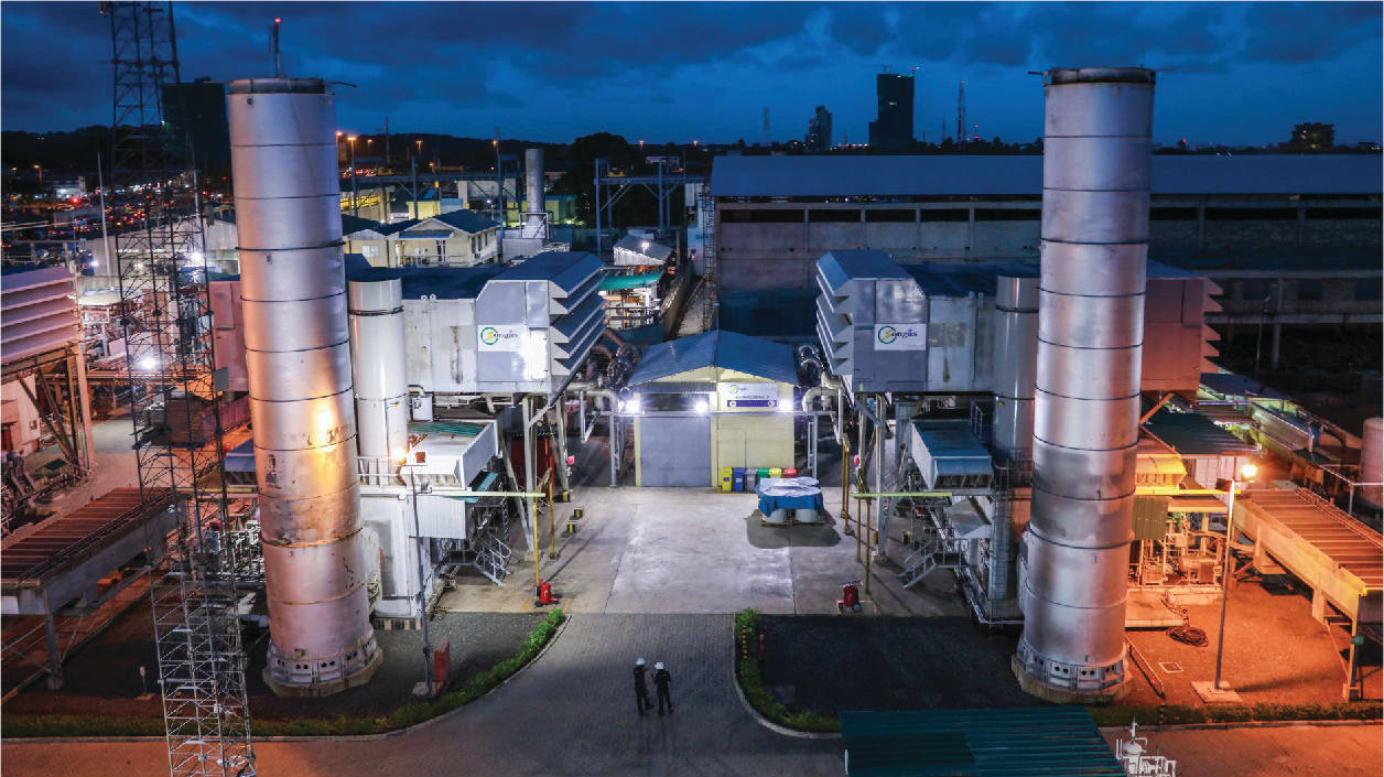 Power plant facility with illuminated towers during evening operations.