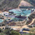 A view of a rare earth mining site surrounded by hills and forested terrain, showing excavation areas and processing pools.