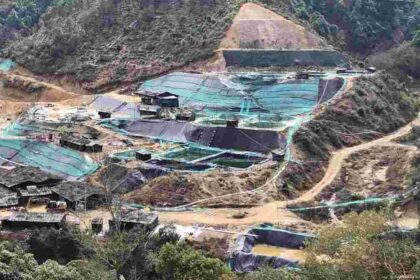 A view of a rare earth mining site surrounded by hills and forested terrain, showing excavation areas and processing pools.