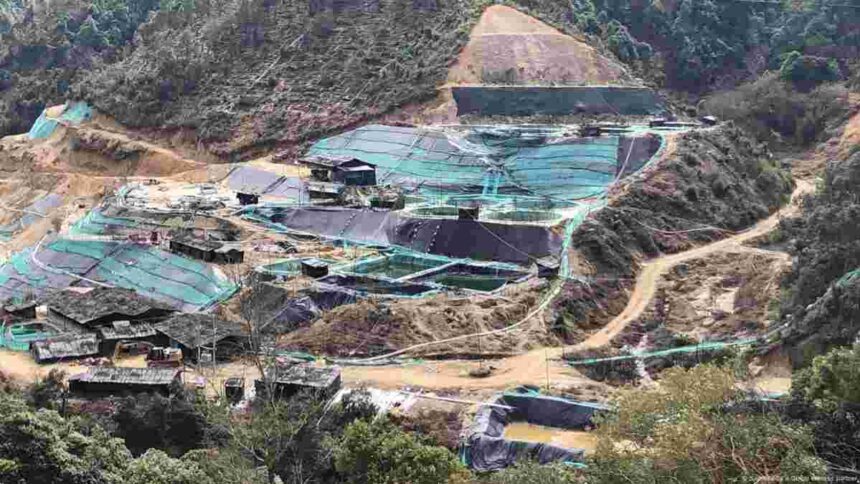 A view of a rare earth mining site surrounded by hills and forested terrain, showing excavation areas and processing pools.