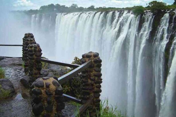 View of Victoria Falls from a wet stone walkway, showing water cascading over the cliff edge amid rising mist.