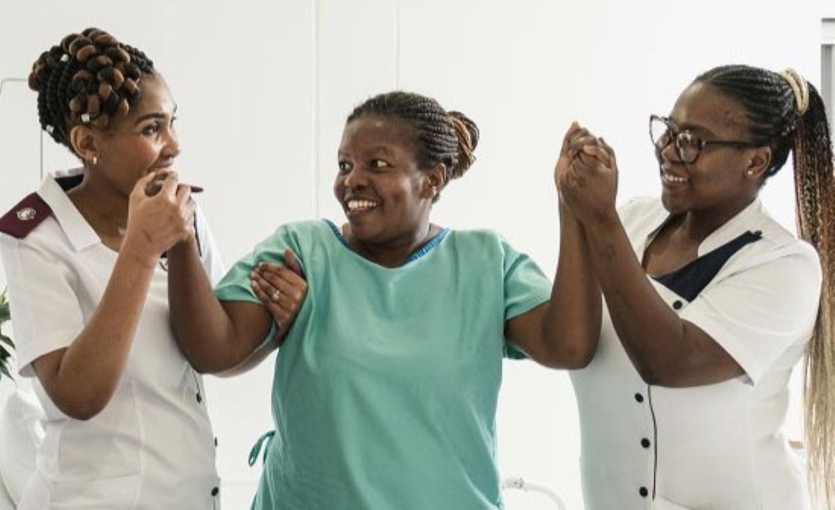 Netcare hospital staff assisting a patient to stand during rehabilitation care at a South African healthcare facility.